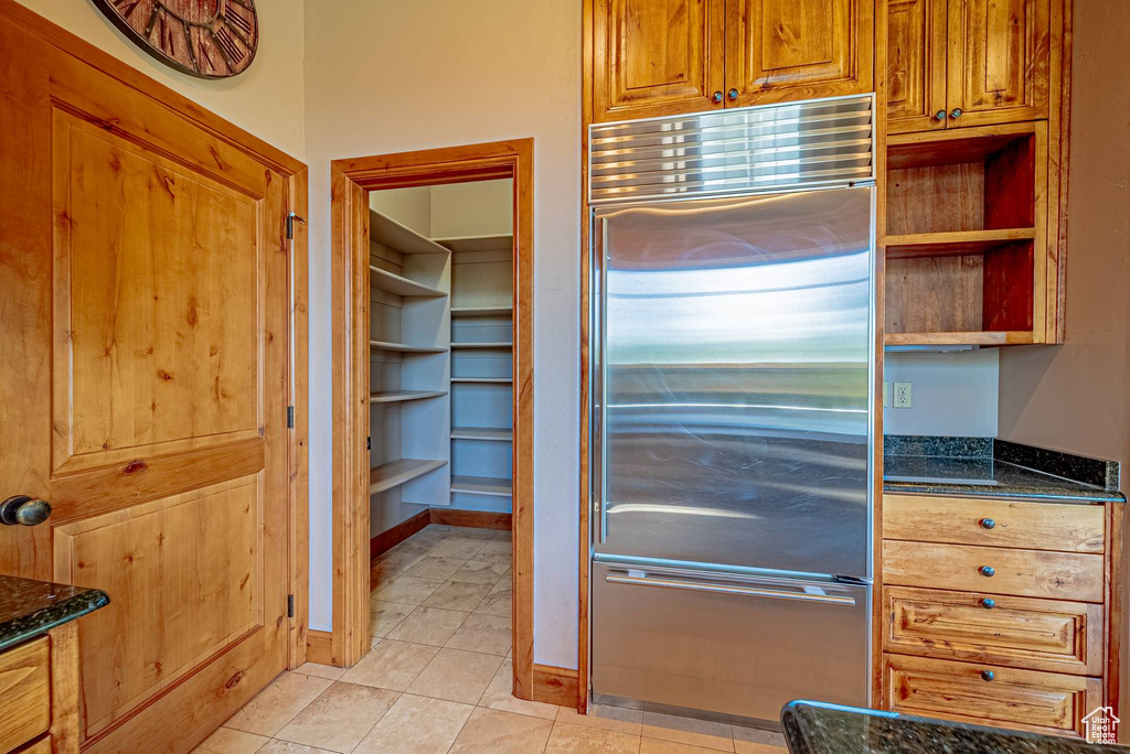 Kitchen featuring built in refrigerator, dark stone counters, brown cabinetry, and light tile patterned flooring