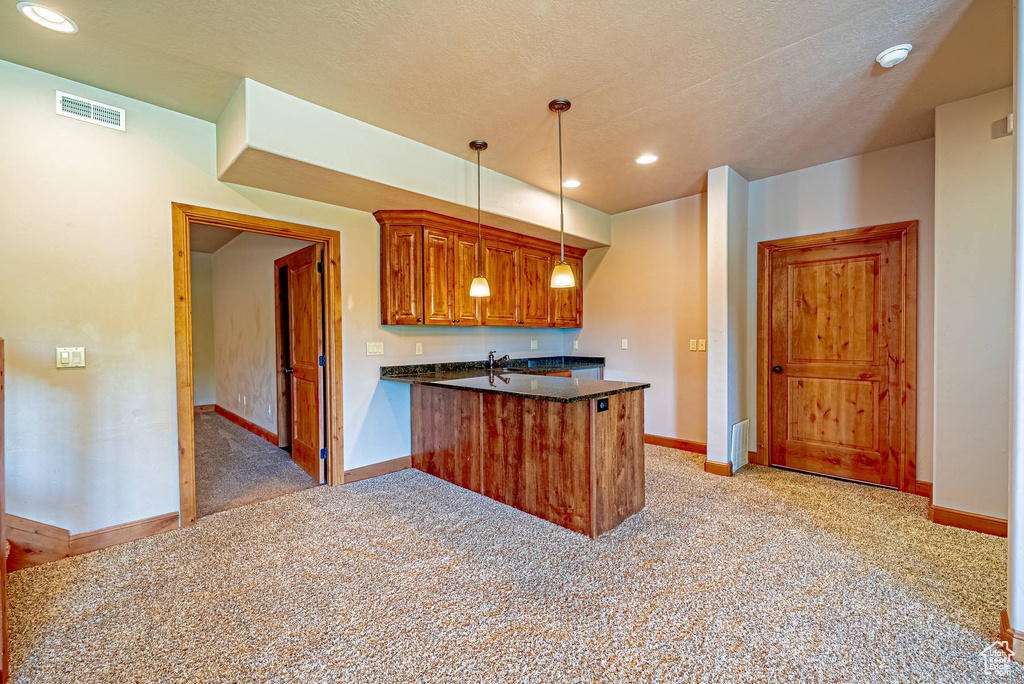 Kitchen with a peninsula, light carpet, baseboards, brown cabinetry, and decorative light fixtures