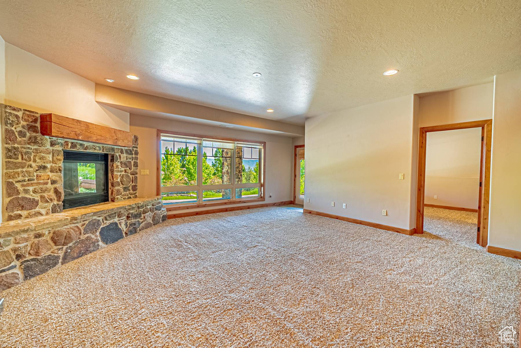 Unfurnished living room featuring carpet, a textured ceiling, baseboards, recessed lighting, and a fireplace