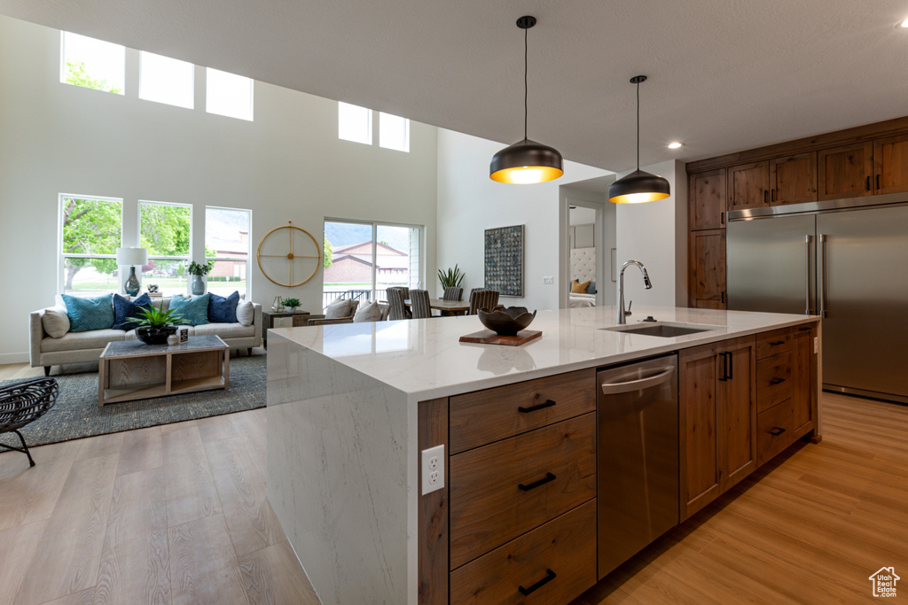 Kitchen with decorative light fixtures, a sink, open floor plan, stainless steel appliances, and light wood-type flooring