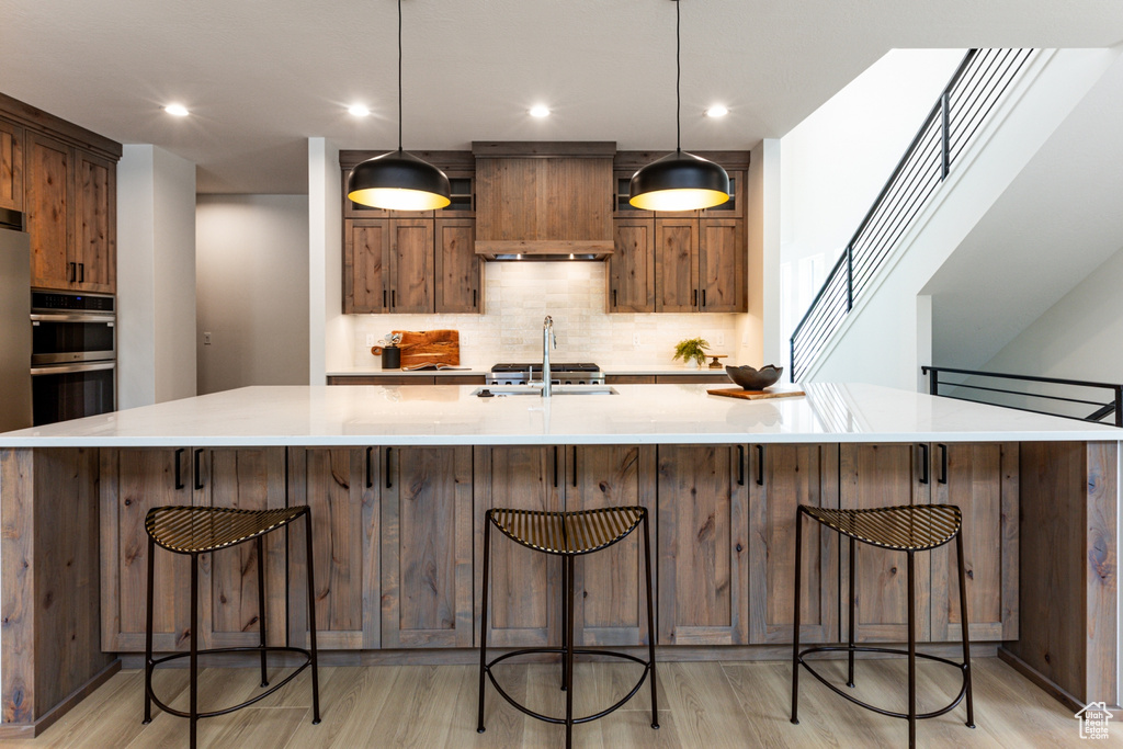 Kitchen with light wood finished floors, tasteful backsplash, a large island with sink, and a sink