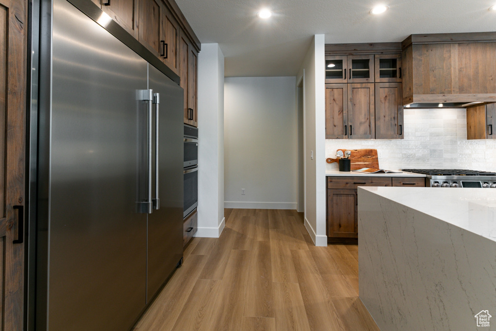 Kitchen with light wood-style flooring, glass insert cabinets, baseboards, tasteful backsplash, and appliances with stainless steel finishes