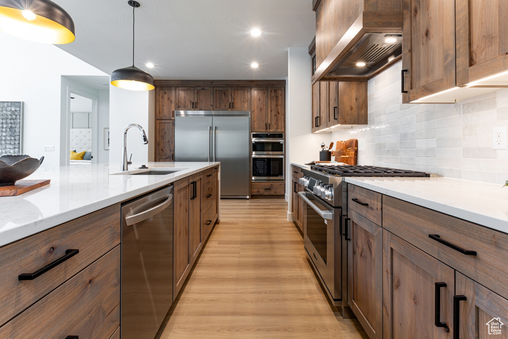 Kitchen featuring light wood finished floors, a sink, high quality appliances, wall chimney range hood, and tasteful backsplash