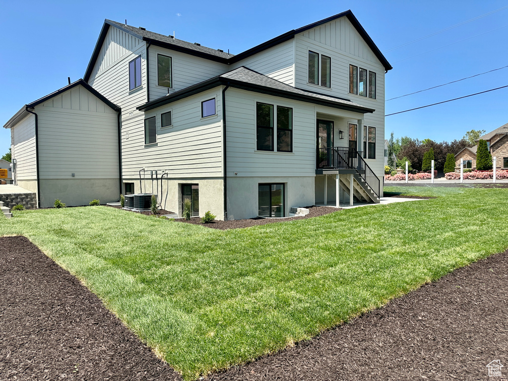 Rear view of house featuring board and batten siding, a lawn, stairway, and central air condition unit