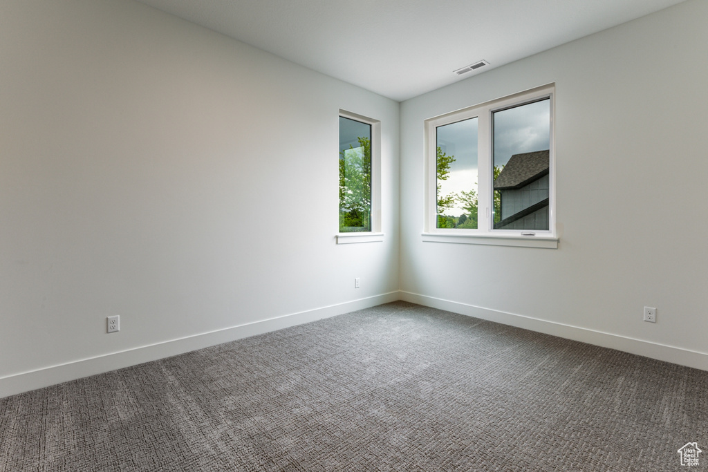 Spare room with baseboards, dark carpet, and visible vents