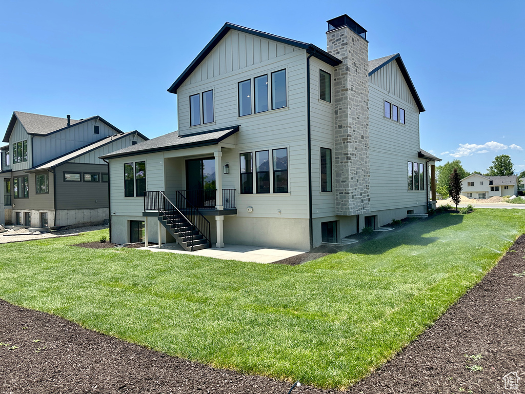 Rear view of property featuring board and batten siding, a chimney, and a yard