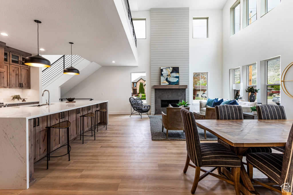 Dining area featuring light wood-style floors, a brick fireplace, recessed lighting, and a high ceiling