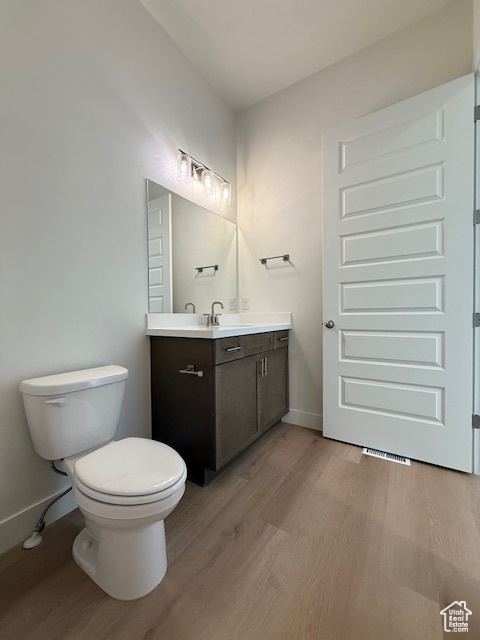 Bathroom with wood finished floors, toilet, vanity, and baseboards