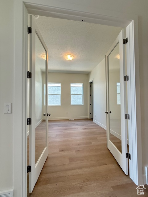 Hallway with french doors, light wood-style floors, baseboards, and a textured ceiling