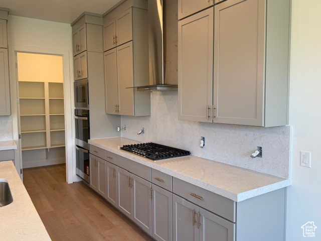 Kitchen with wall chimney exhaust hood, stainless steel appliances, gray cabinetry, light countertops, and decorative backsplash