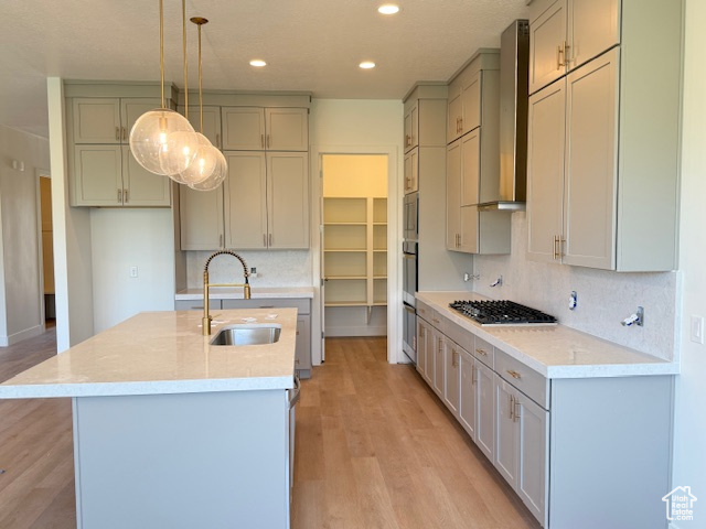 Kitchen with a sink, wall chimney exhaust hood, gas cooktop, tasteful backsplash, and light wood-style floors