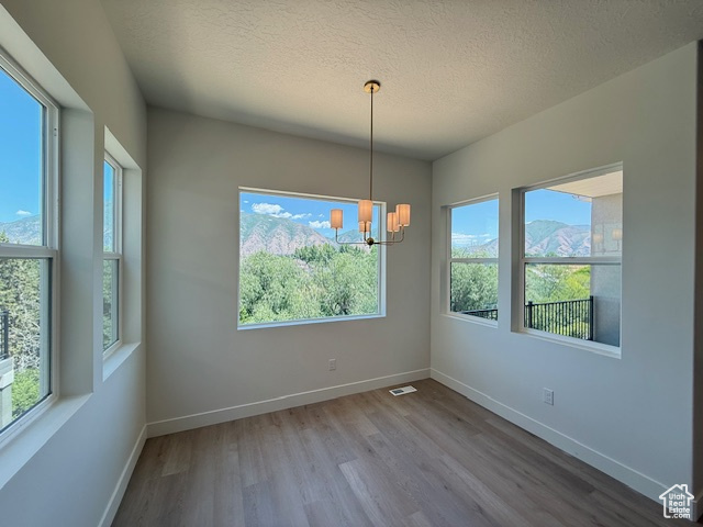 Unfurnished room featuring a chandelier, wood finished floors, plenty of natural light, baseboards, and a textured ceiling