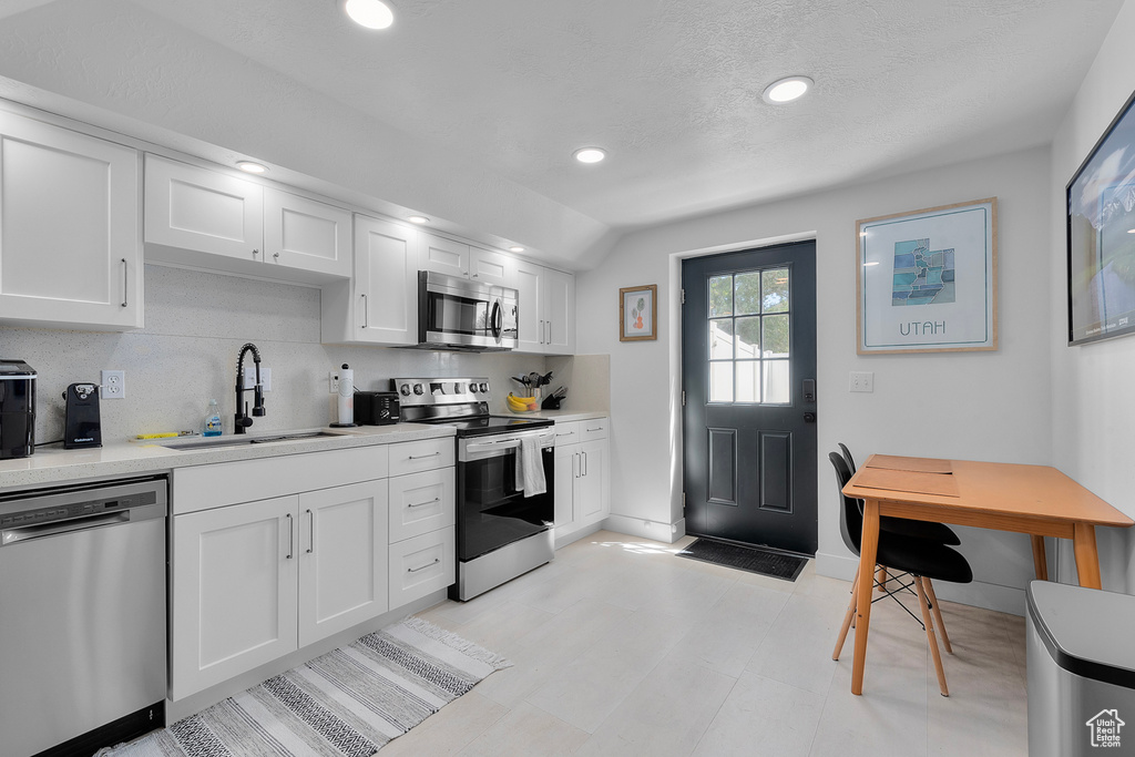 Kitchen with stainless steel appliances, a sink, light countertops, baseboards, and recessed lighting
