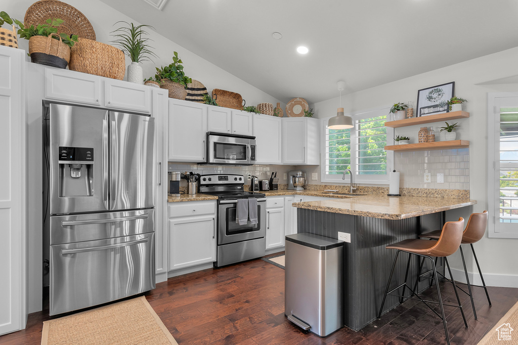 Kitchen featuring stainless steel appliances, a peninsula, decorative backsplash, white cabinets, and healthy amount of natural light