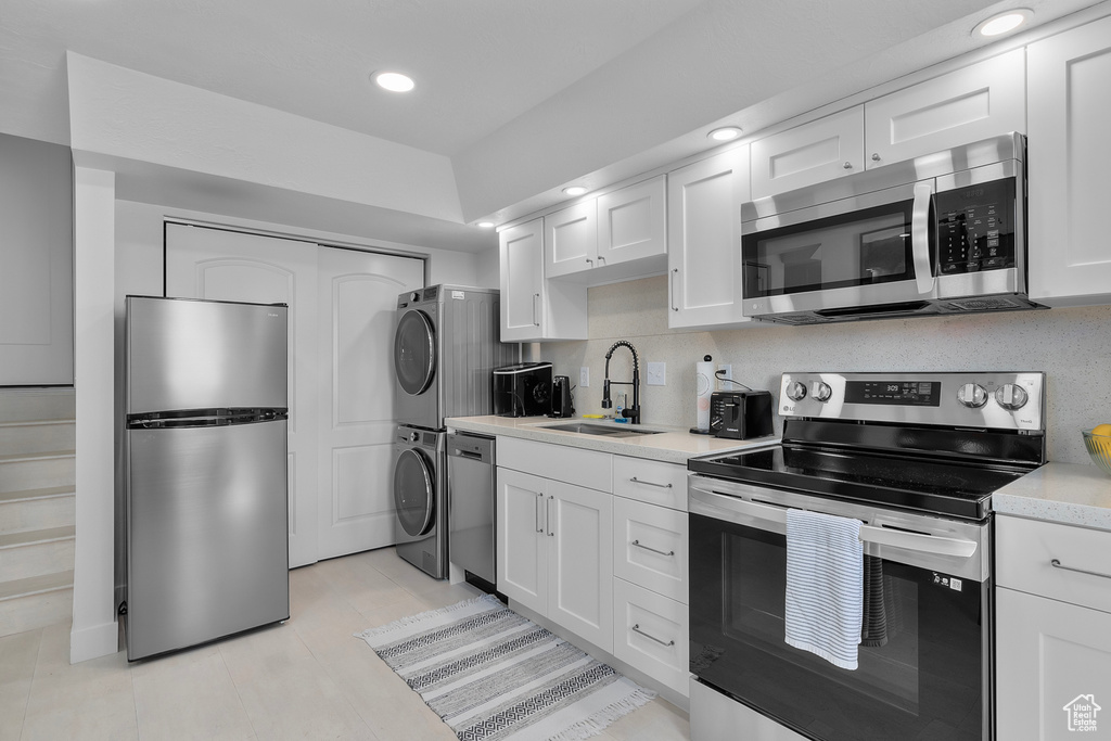 Kitchen with appliances with stainless steel finishes, stacked washer / dryer, a sink, light countertops, and white cabinets