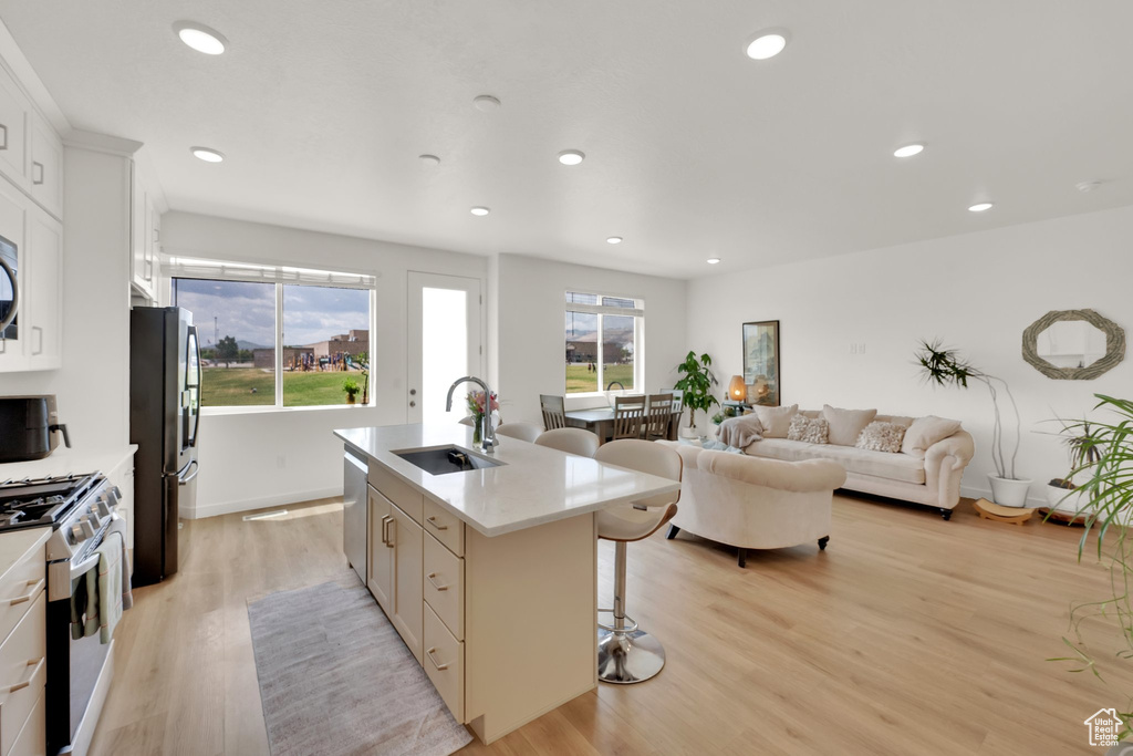 Kitchen featuring a sink, stainless steel appliances, a breakfast bar area, a kitchen island with sink, and light wood-type flooring