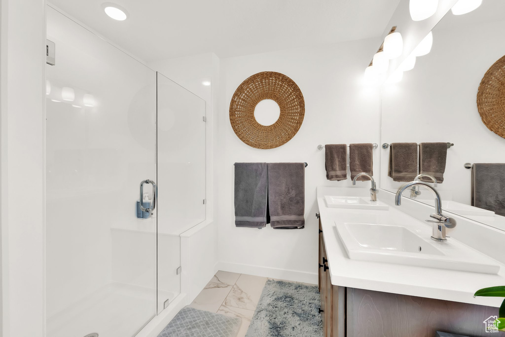 Full bathroom with marble finish flooring, double vanity, a stall shower, and baseboards