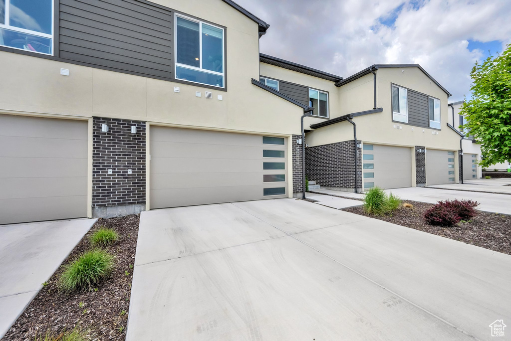 View of front of property featuring a garage, stucco siding, brick siding, and driveway