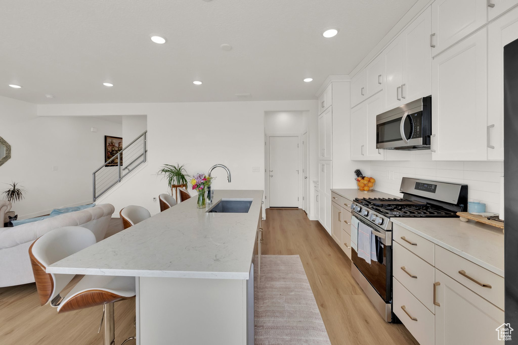 Kitchen with stainless steel appliances, a sink, a breakfast bar, light wood finished floors, and recessed lighting