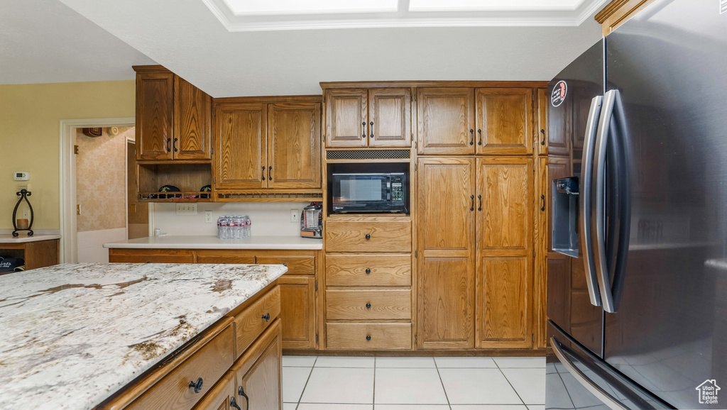Kitchen featuring stainless steel refrigerator with ice dispenser, black microwave, light tile patterned floors, brown cabinetry, and open shelves