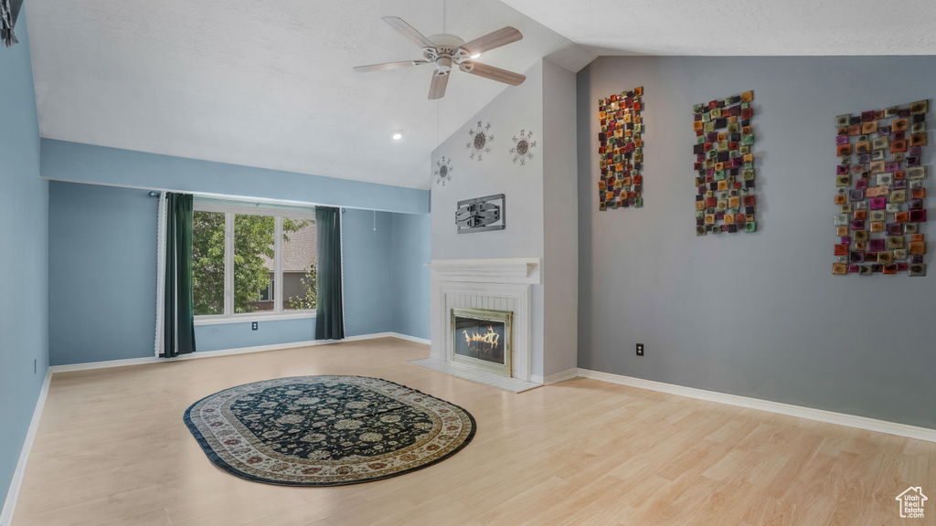 Living room featuring a ceiling fan, wood finished floors, a glass covered fireplace, high vaulted ceiling, and baseboards