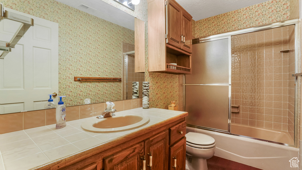 Bathroom featuring wallpapered walls, vanity, toilet, and combined bath / shower with glass door