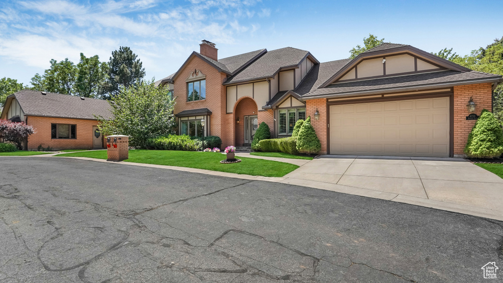 English style home featuring concrete driveway, brick siding, a chimney, and an attached garage