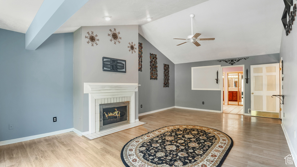 Living area with ceiling fan, light wood-style flooring, a tiled fireplace, vaulted ceiling, and baseboards