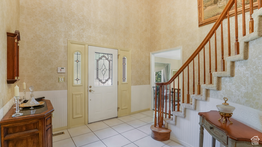 Entrance foyer with stairs, light tile patterned floors, a wainscoted wall, and a towering ceiling