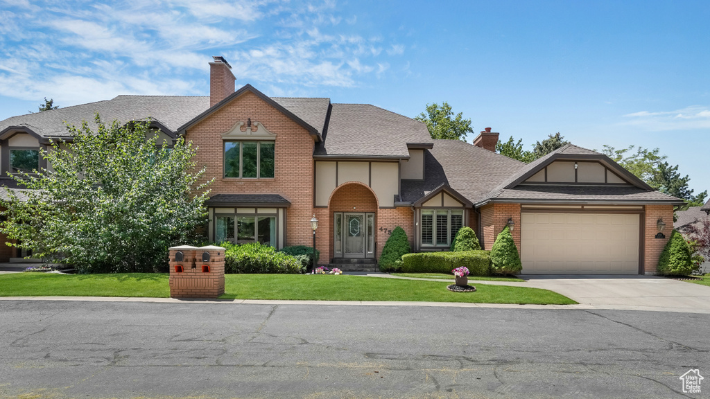 Tudor home with a chimney, an attached garage, a front yard, and concrete driveway