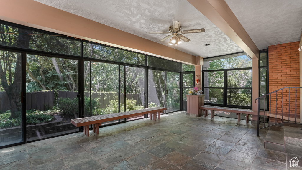 Unfurnished sunroom featuring stone tile flooring, a ceiling fan, and a textured ceiling