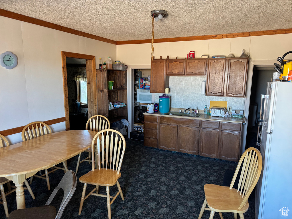 Kitchen with white appliances, a textured ceiling, ornamental molding, dark colored carpet, and a sink