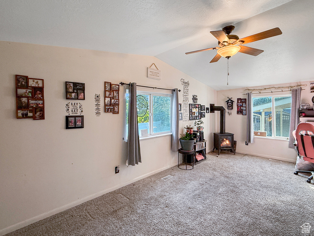Office featuring a wood stove, lofted ceiling, ceiling fan, carpet flooring, and healthy amount of natural light
