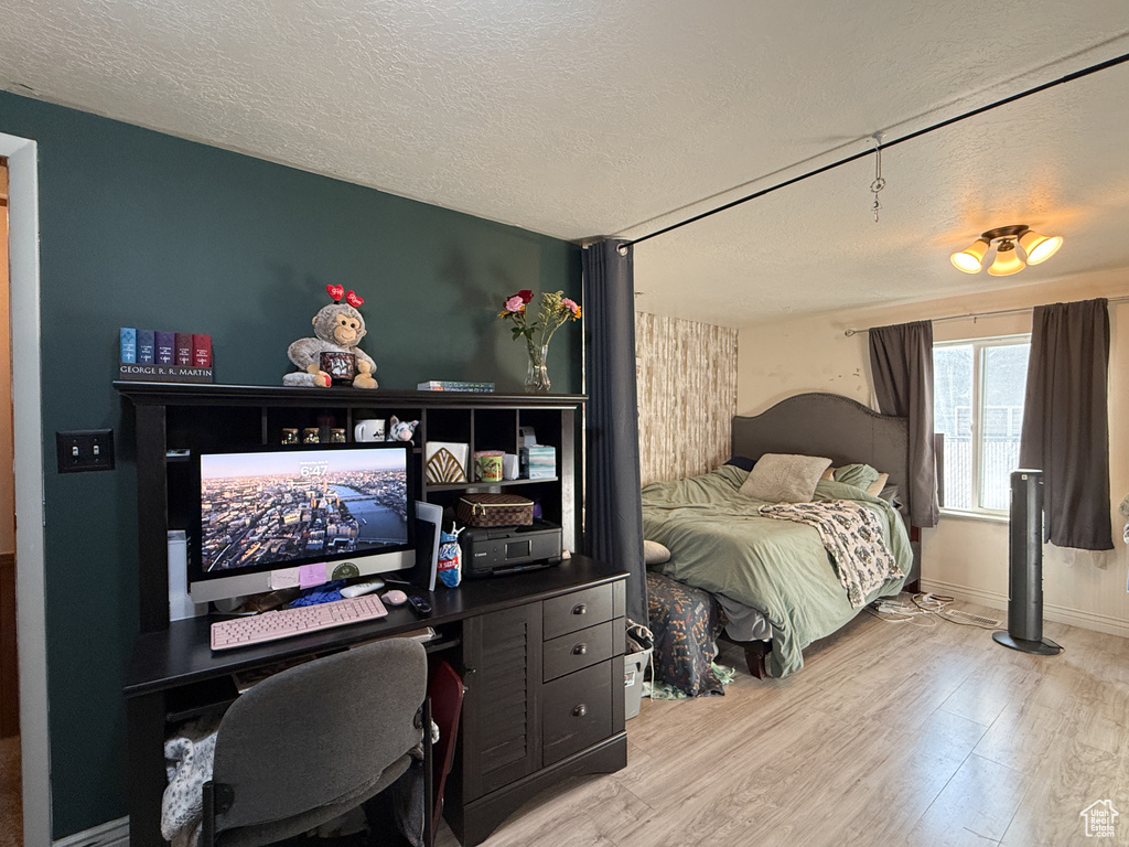Bedroom with a textured ceiling, wood finished floors, and an office area