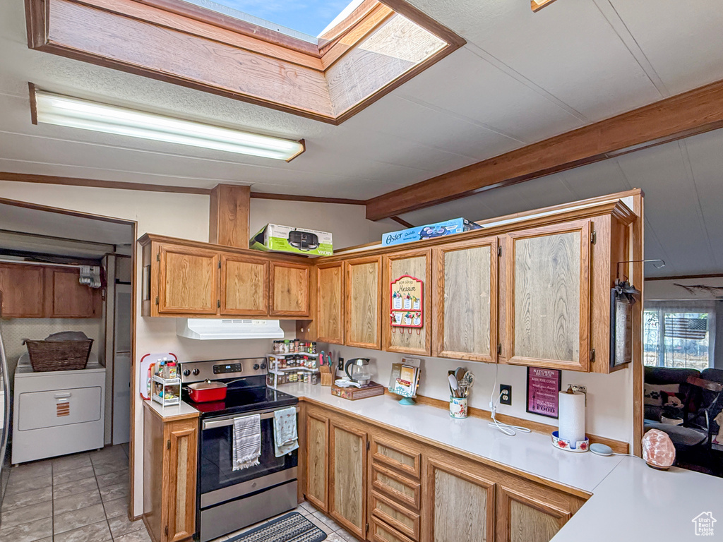 Kitchen featuring electric stove, washer / dryer, light countertops, under cabinet range hood, and light tile patterned flooring