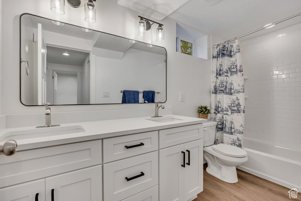 Bathroom with double vanity, toilet, shower / tub combo, and wood finished floors