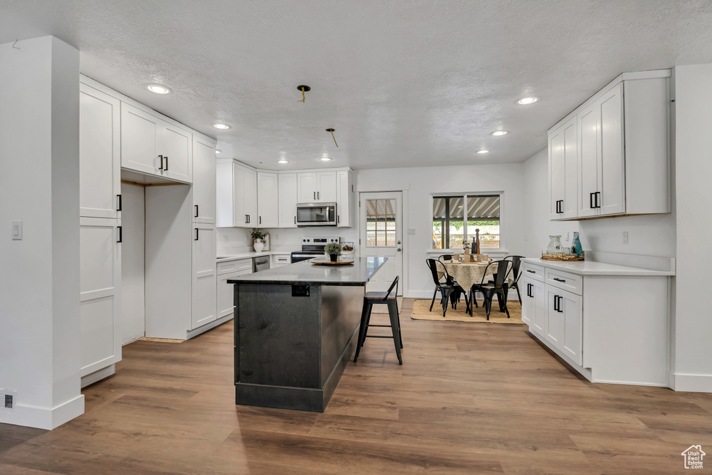 Kitchen with appliances with stainless steel finishes, recessed lighting, baseboards, white cabinets, and wood finished floors