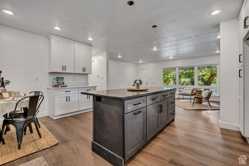 Kitchen featuring light wood finished floors, white cabinets, a center island, baseboards, and recessed lighting