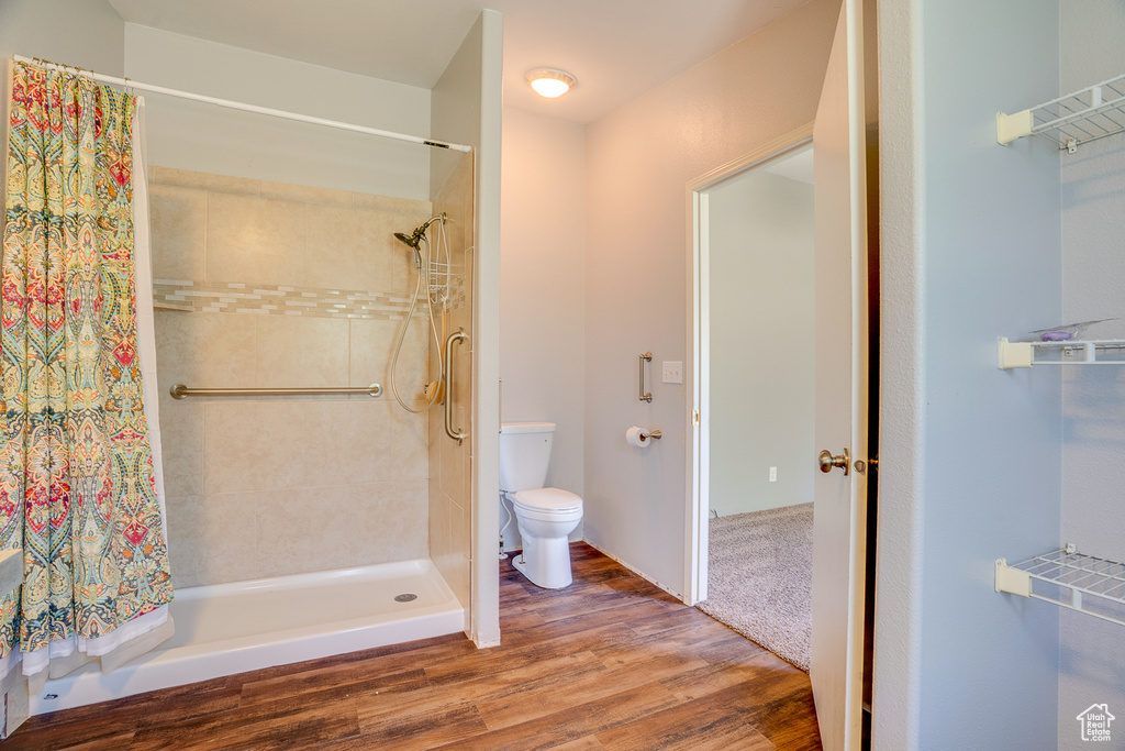Full bath featuring toilet, tiled shower, and wood finished floors