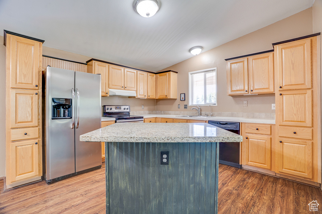 Kitchen featuring stainless steel appliances, light brown cabinetry, under cabinet range hood, a sink, and wood finished floors