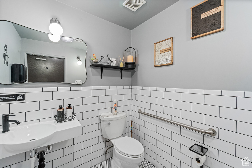 Bathroom featuring toilet, tile walls, a sink, and a wainscoted wall