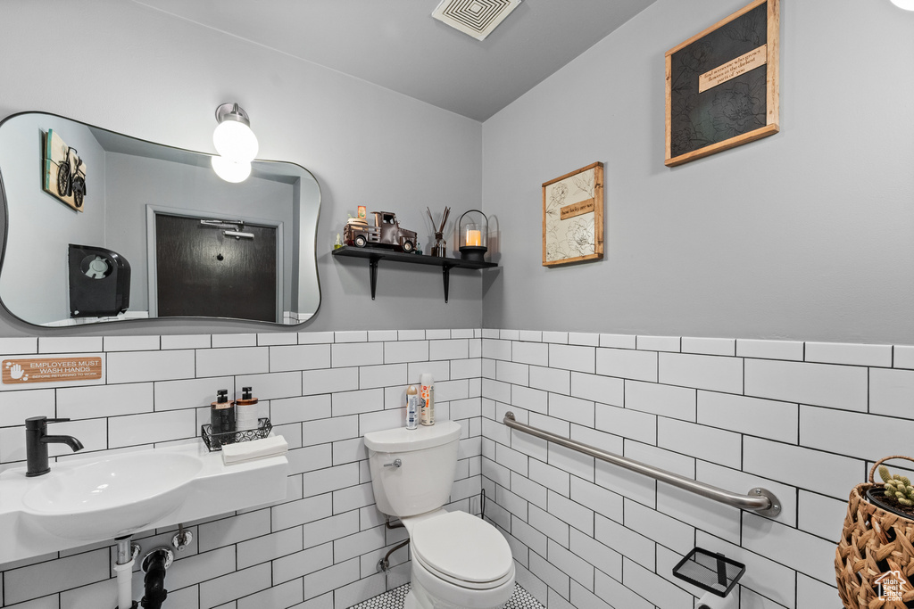 Bathroom with toilet, tile walls, a sink, and wainscoting