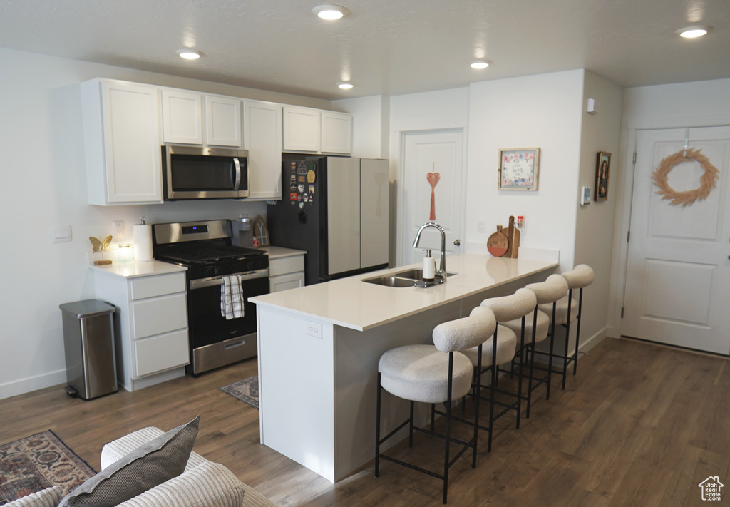 Kitchen featuring appliances with stainless steel finishes, a sink, a breakfast bar, white cabinetry, and recessed lighting