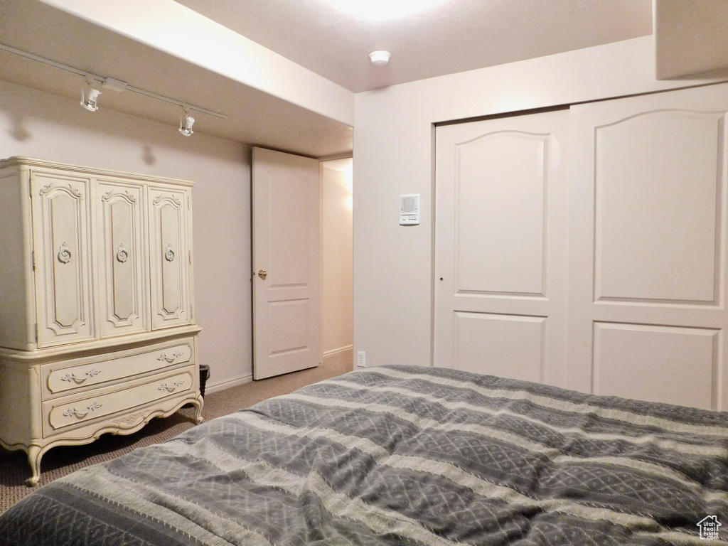 Bedroom with light colored carpet, track lighting, a closet, and baseboards