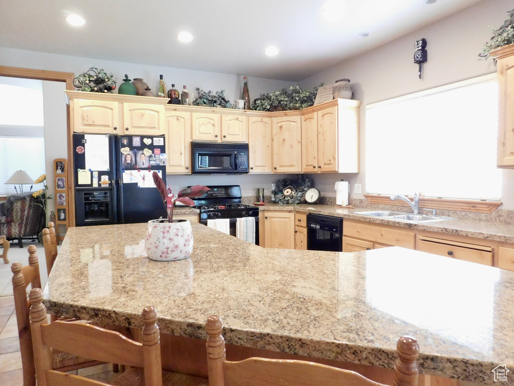 Kitchen with black appliances, a sink, light brown cabinets, a kitchen bar, and recessed lighting