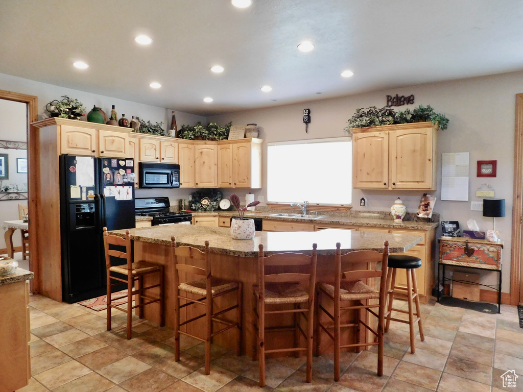 Kitchen featuring black appliances, light brown cabinetry, a sink, recessed lighting, and a center island