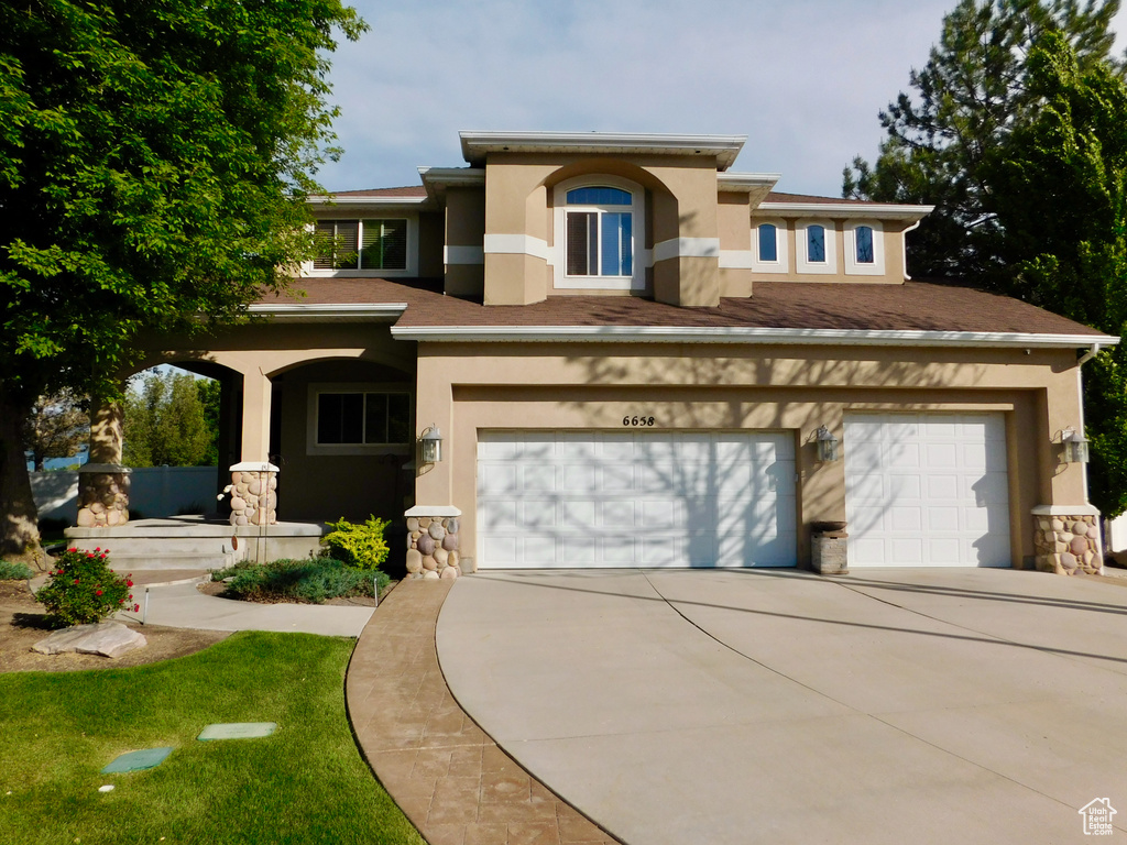 View of front of house with stucco siding, driveway, an attached garage, stone siding, and a porch