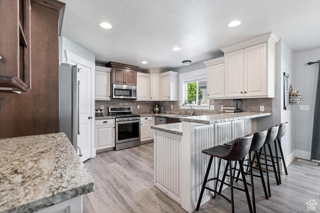 Kitchen featuring appliances with stainless steel finishes, a peninsula, a sink, light wood finished floors, and recessed lighting