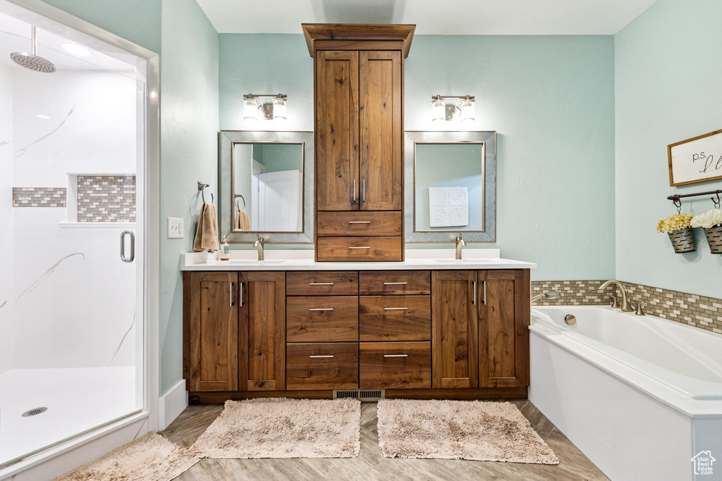 Full bath featuring a stall shower, double vanity, a garden tub, and wood finished floors