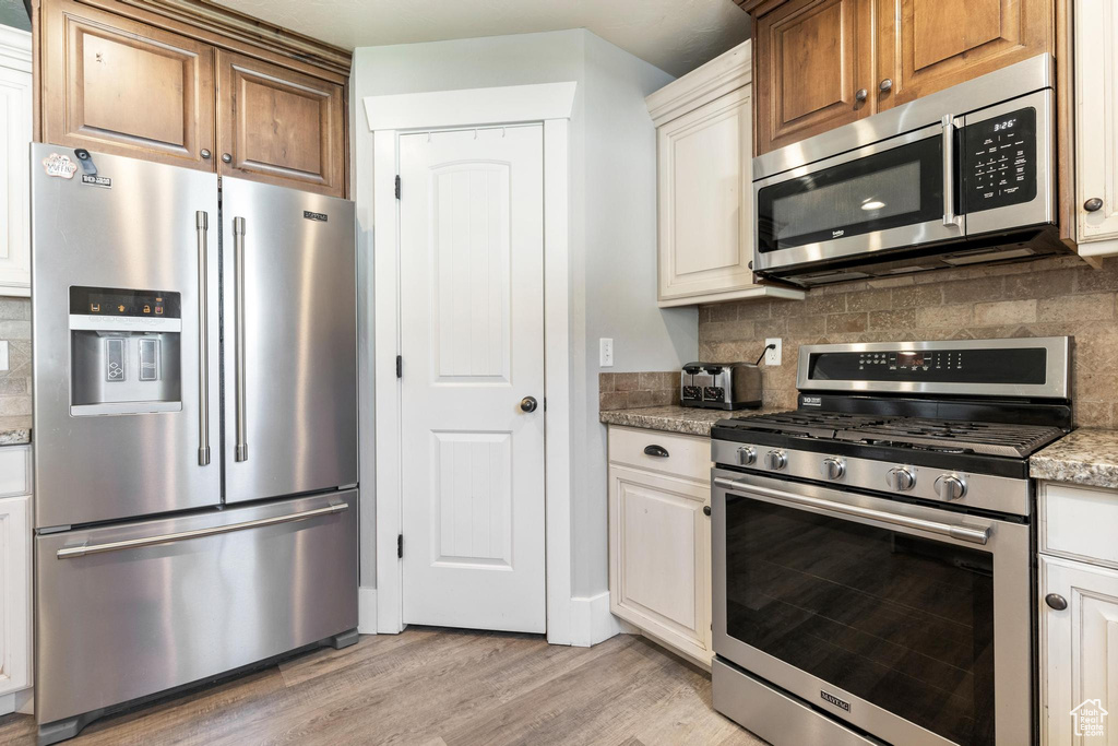 Kitchen with appliances with stainless steel finishes, light wood finished floors, backsplash, and light stone countertops